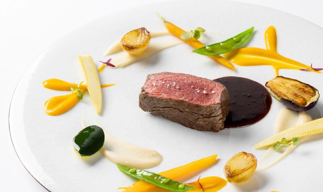 A plate with meat, vegetables, and dark sauce, arranged artfully.