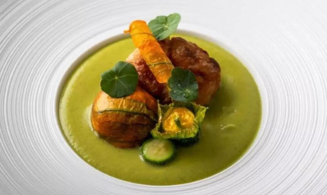 A dish with crispy chicken on green sauce, garnished with herbs and an orange slice.