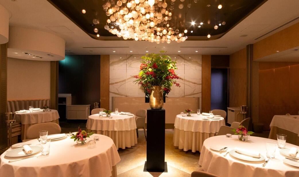 A restaurant interior with round tables, a chandelier, and a central floral display.