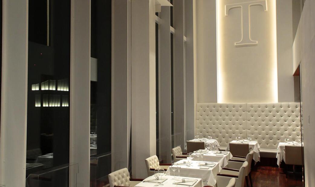 A modern restaurant with tall windows and tufted white seating.