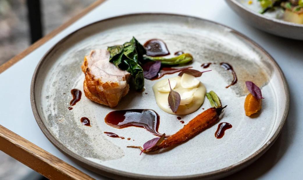 Roasted pork belly with vegetables and sauces on a ceramic plate