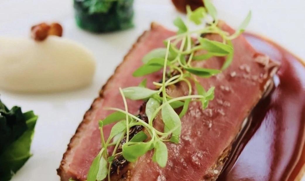 A close-up of thinly sliced meat with sauce and herbs, showcasing its tenderness.