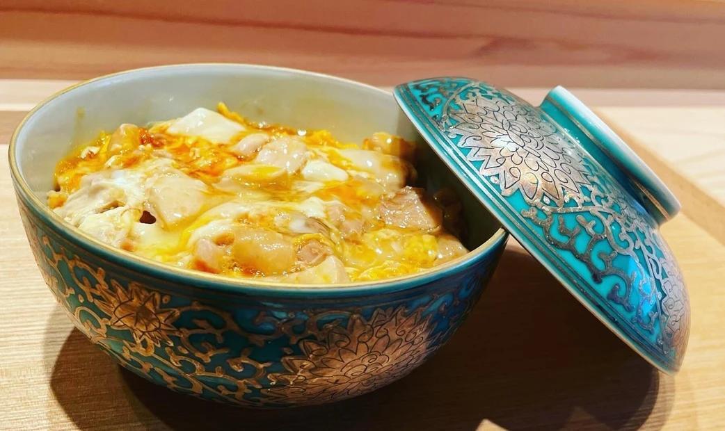 A bowl of simmered chicken and eggs, served in a decorative blue bowl with a partially open lid.