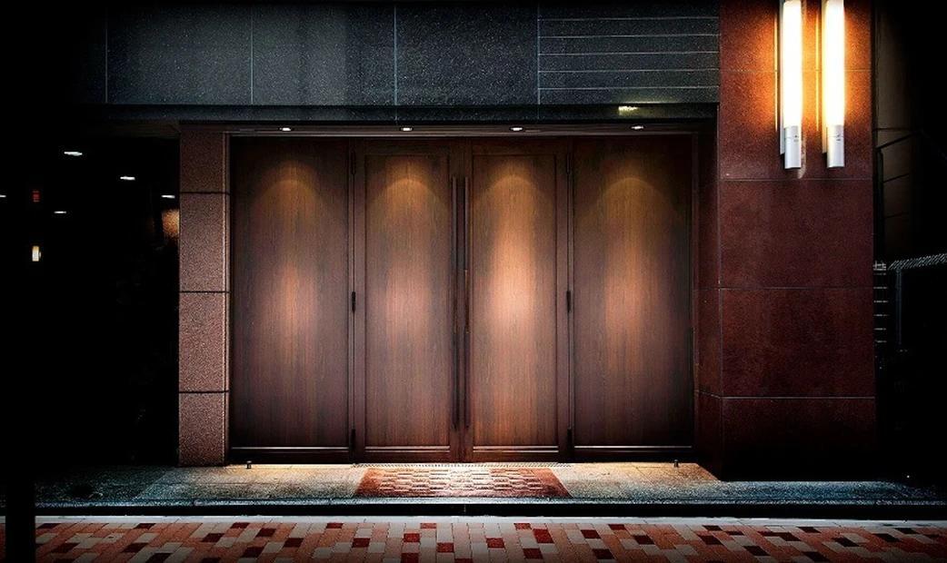 The entrance of a restaurant with large wooden doors, illuminated by soft lighting.