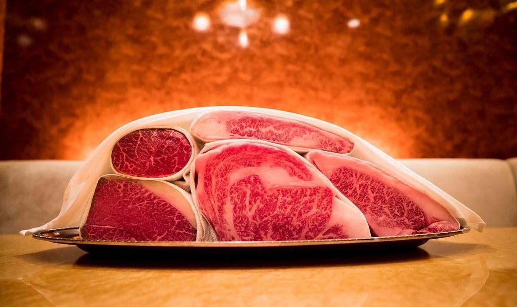 A display of various cuts of marbled wagyu beef, presented on a platter with a warm background.