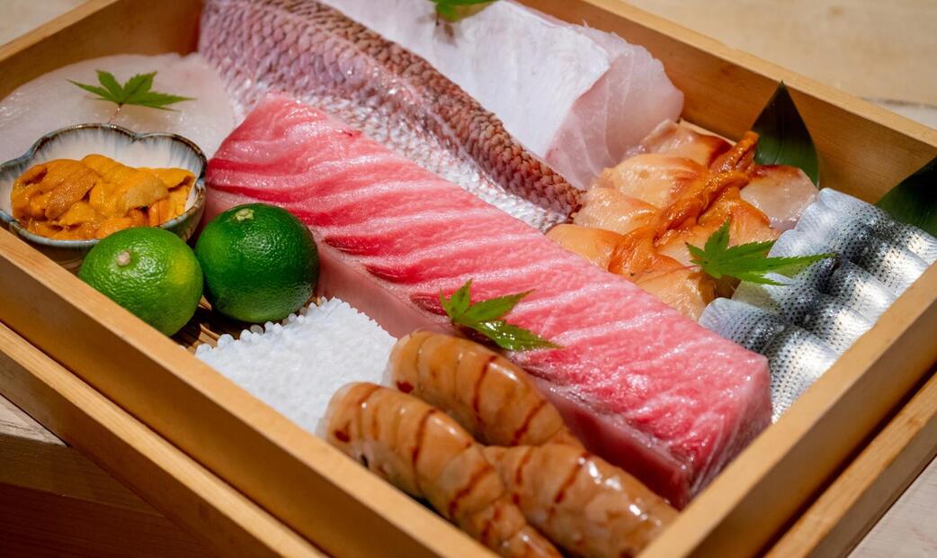  A wooden box filled with fresh seafood, including tuna, prawns, and garnishes.